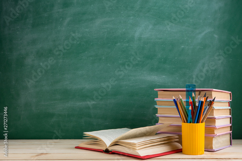 Education and reading concept - group of colorful books on the wooden table in the classroom, blackboard background