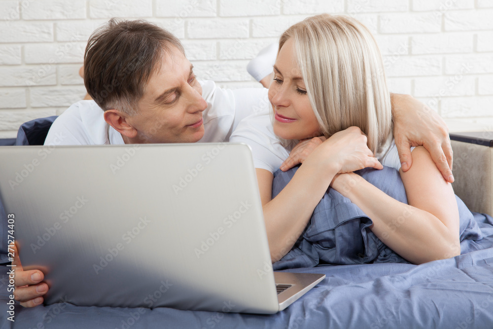Cute couple relaxing on bed using laptop at home in the bedroom Cute couple relaxing on bed using laptop at home in the bedroom