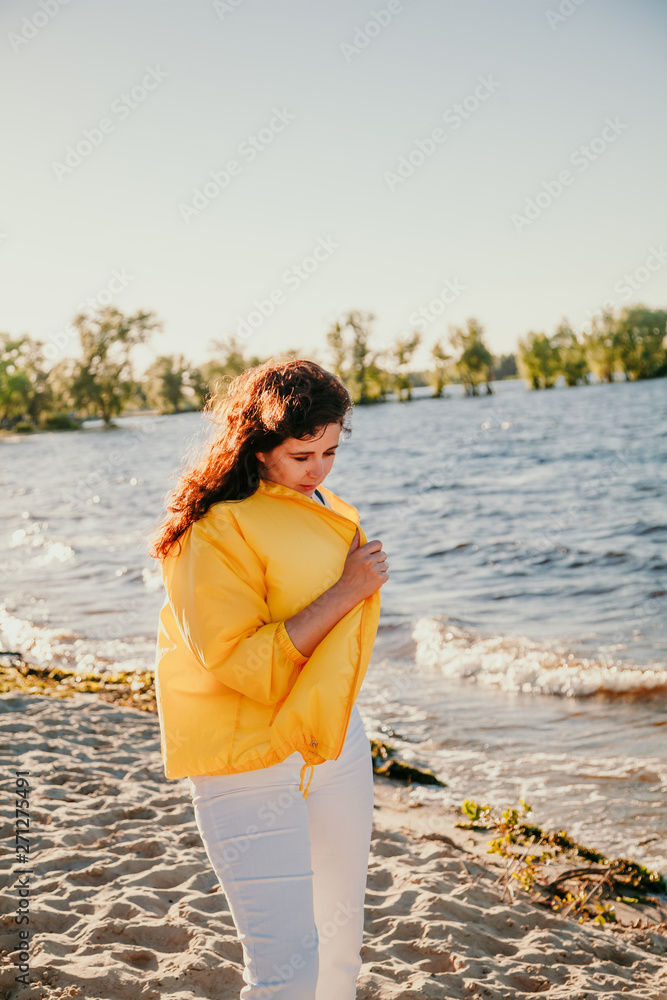 Beautiful plus size woman in yellow jacket on sandy shore