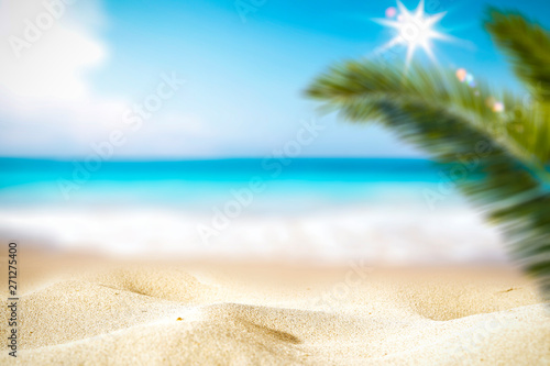 Summer background of hot sand with free space for your decoration and blurred background of ocean with green palm and sun light. 
