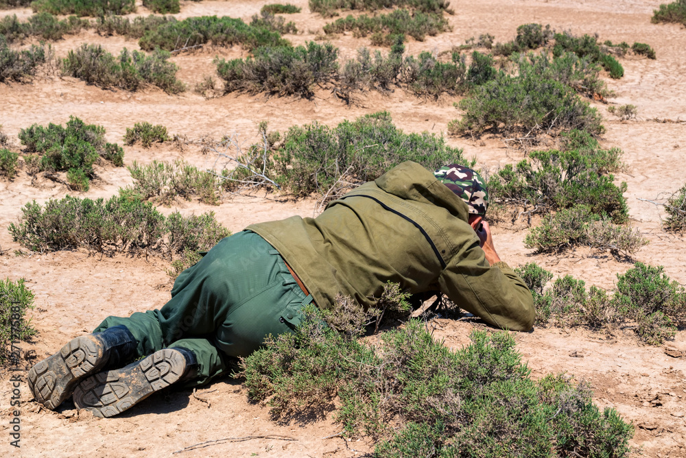 Back view outdoor photographer lies on ground taking picture of lizard in steppe Back view outdoor photographer lies on ground taking picture of lizard in steppe
