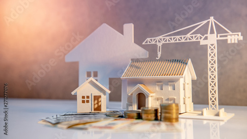 Real estate or property development. Construction business investment concept. Home mortgage loan rate. Coin stack on international banknotes with house and construction crane models on the table. photo