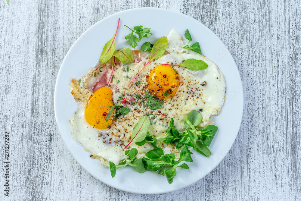 Plate of fried egg with bacon ancd melted cheese, on white plate, top view on vintage wooden background