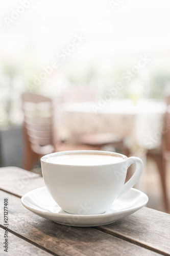 a white coffee mug stands on a wooden table in an outdoor coffee shop. light blurred background. close up, vertical photo