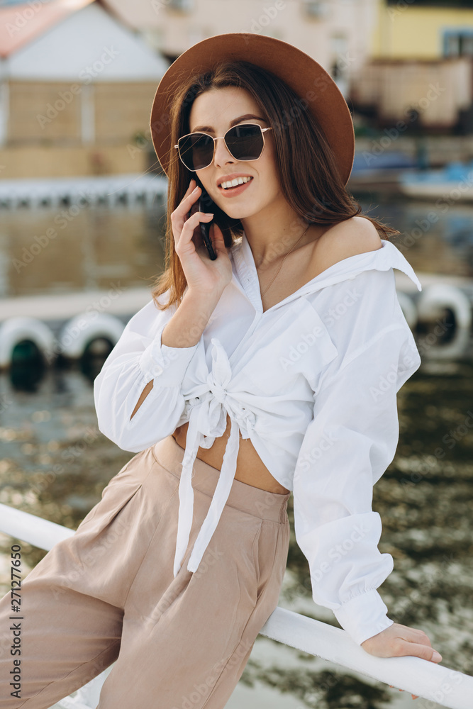 A stylish woman talking by phone and walking along the beachfront on a warm summer day at sunset