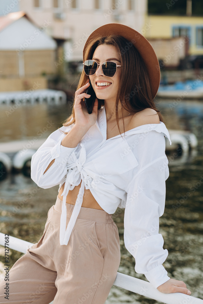 A stylish woman talking by phone and walking along the beachfront on a warm summer day at sunset