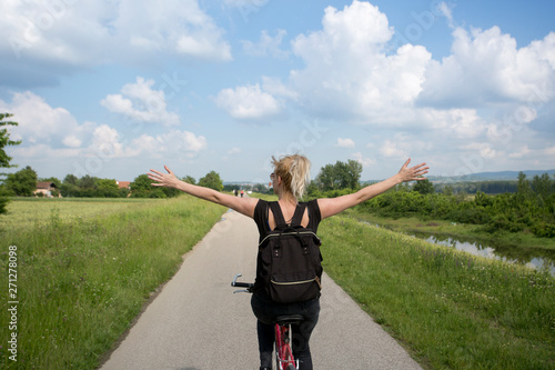 Young beautiful woman riding bicycle and spreading arms in countryside.