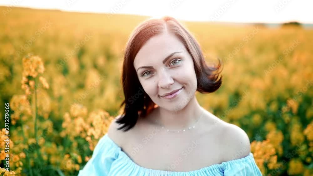 Portrait of young pretty woman in blue dress posing in rapeseed yellow flowers field. Spring time, sunset light. Portrait of young pretty woman in blue dress posing in rapeseed yellow flowers field. Spring time, sunset light.