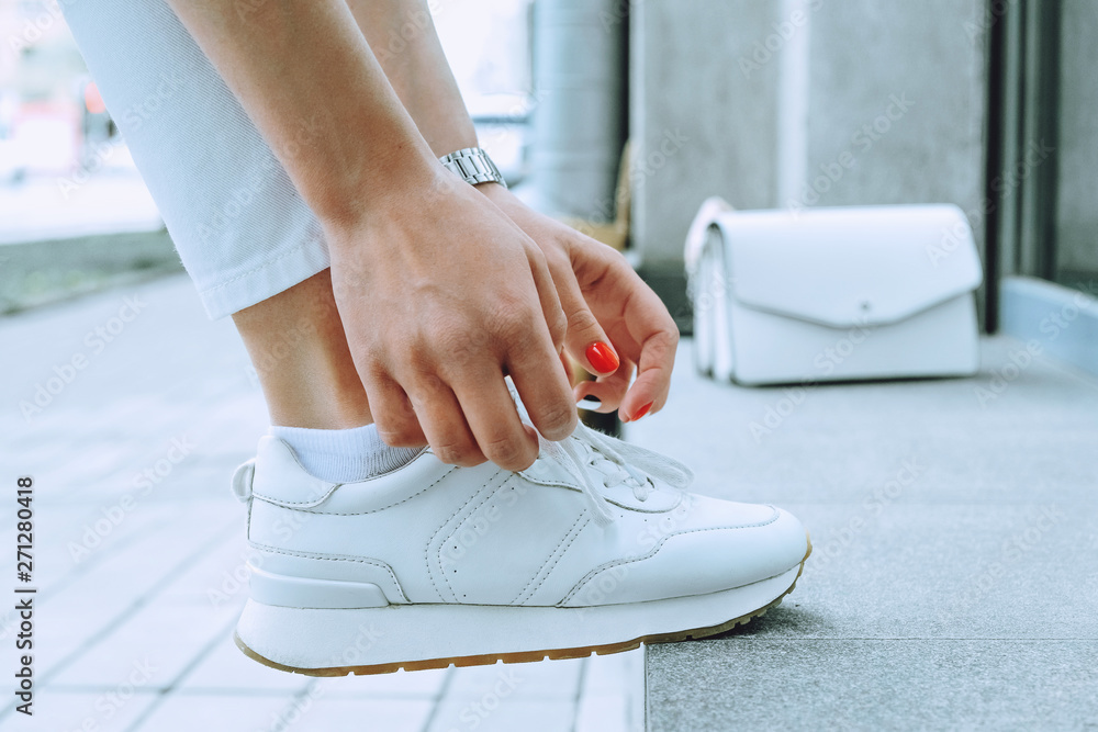 Fototapeta premium Legs of young girl in white sneakers close up, girl tying shoelaces