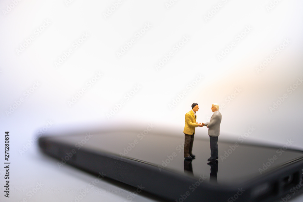 Technology and Business concept. Two businessman miniature people figures standing, talking and hand shake on smart mobile phone. Technology and Business concept. Two businessman miniature people figures standing, talking and hand shake on smart mobile phone.