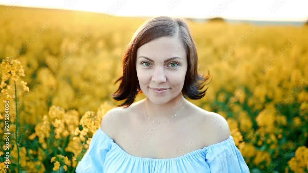 Portrait of young pretty woman in blue dress posing in rapeseed yellow flowers field. Spring time, sunset light. Portrait of young pretty woman in blue dress posing in rapeseed yellow flowers field. Spring time, sunset light.