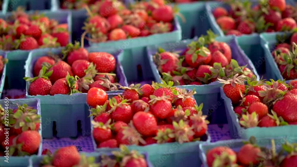 Slide to right showing fresh strawberries in cardboard boxes as hand adjusts them at a farmers market. Slide to right showing fresh strawberries in cardboard boxes as hand adjusts them at a farmers market.