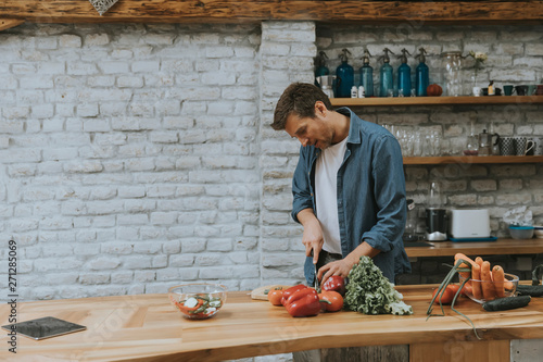 Fototapeta Young man chopping vegetables in the kitchen and preparing healthy meal