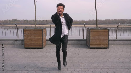 Closeup straight view portrait of young attractive african american businessman dancing and making shuffle moves looking at camera on the street in the urban city photo