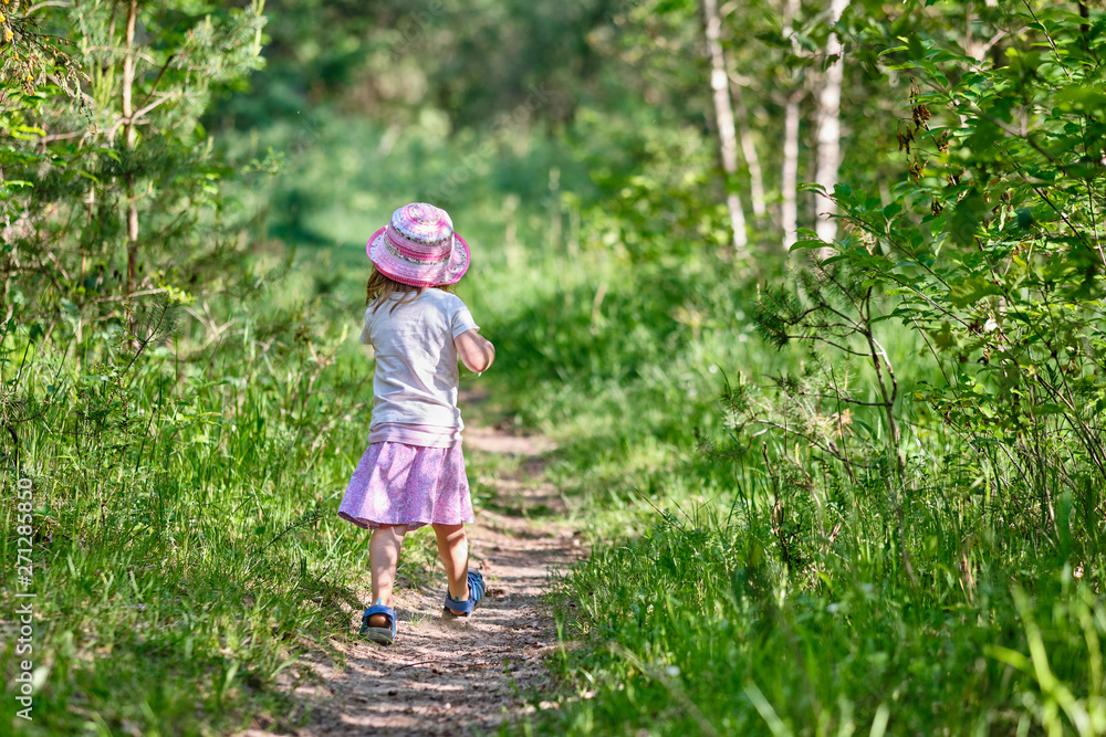Rear view of young 3 year old girl with water bottle in her hand walking on a narrow path in the green summer forest Rear view of young 3 year old girl with water bottle in her hand walking on a narrow path in the green summer forest
