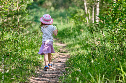 Rear view of young 3 year old girl with water bottle in her hand walking on a narrow path in the green summer forest © franconiaphoto