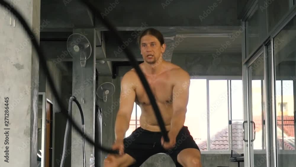 Slow motion shot of Muscular powerful young man training with battle rope doing exercise in functional training fitness gym. Caucasian male fit model working out indoors Slow motion shot of Muscular powerful young man training with battle rope doing exercise in functional training fitness gym. Caucasian male fit model working out indoors