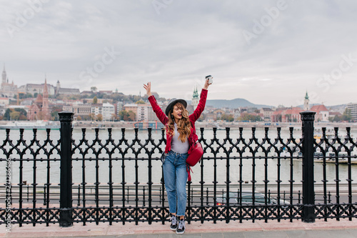 Photography Full-length portrait of blissful caucasian lady in red jacket posing with hands up on embankment