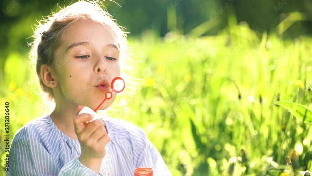 Beautiful little girl at sunny summer day blowing soap bubbles green meadow. Summer fun concept. Slow motion. Beautiful little girl at sunny summer day blowing soap bubbles green meadow. Summer fun concept. Slow motion.