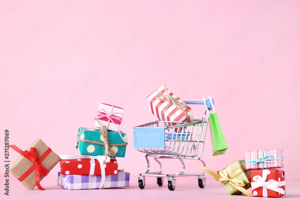 Fototapeta Small shopping cart with gift boxes on pink background