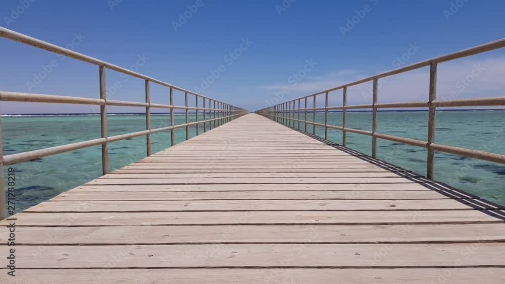 Perspective view of a wooden pier in the sea, against a clear blue sky Perspective view of a wooden pier in the sea, against a clear blue sky