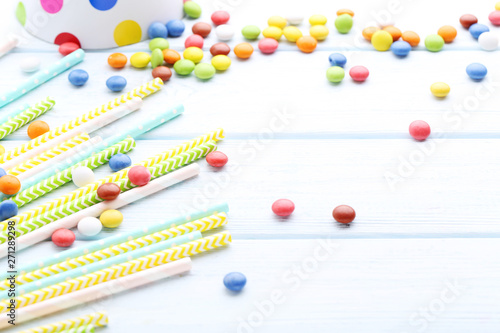 Colorful paper straws with candies on wooden table