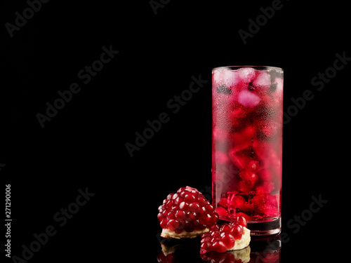 Sweet pomegranate with ice and berry on black background. Delicious summer red lemonade/cold tea.