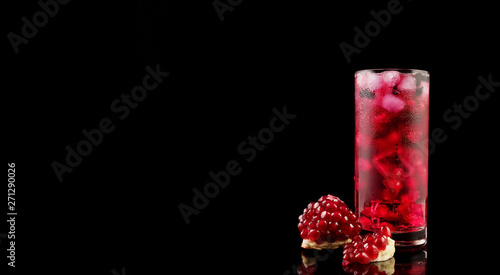 Sweet pomegranate with ice and berry on black background. Delicious summer red lemonade/cold tea.