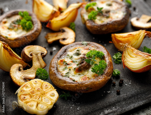Baked portobello mushrooms stuffed with cheese and herbs on a black background, close-up. Vegetarian food photo
