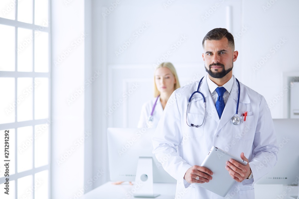 Confident smiling doctor posing and looking at camera with arms crossed, medical staff working on the background Confident smiling doctor posing and looking at camera with arms crossed, medical staff working on the background