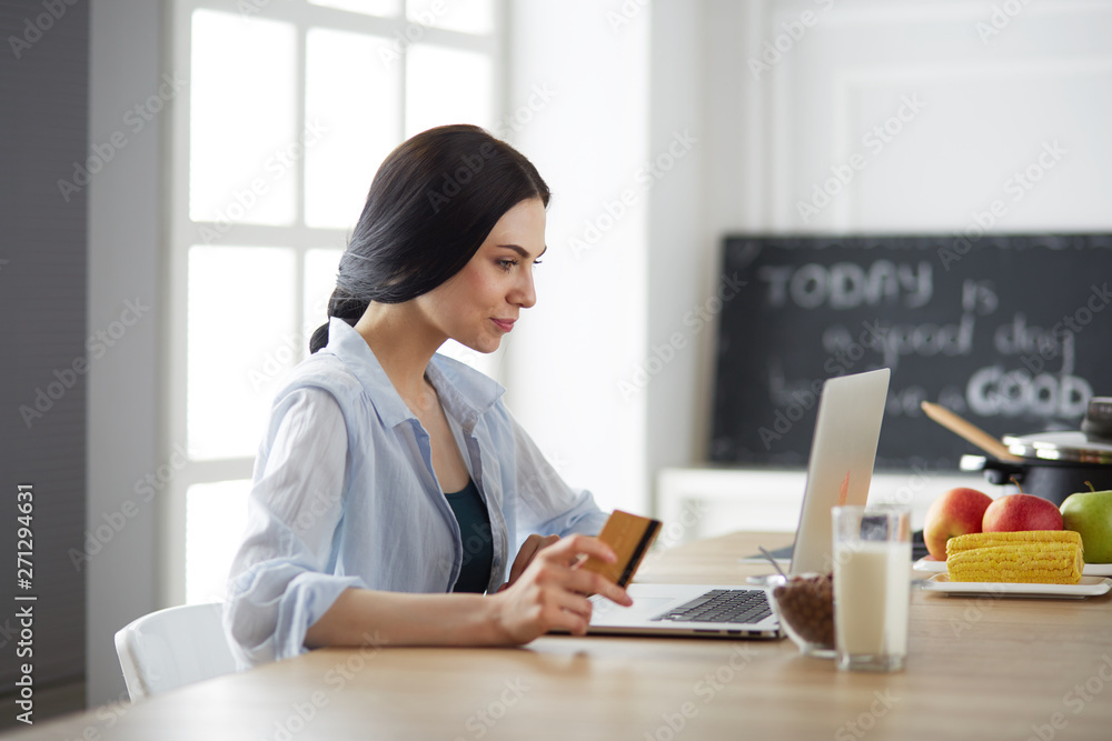 Smiling woman online shopping using tablet and credit card in kitchen Smiling woman online shopping using tablet and credit card in kitchen