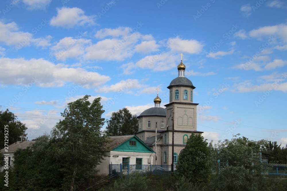 Spring landscape with a rural church under a blue sky with white clouds in Chuvashia