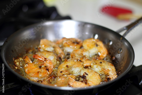 Shrimp scampi cooking in butter and garlic in a stainless steel skillet on the stove.