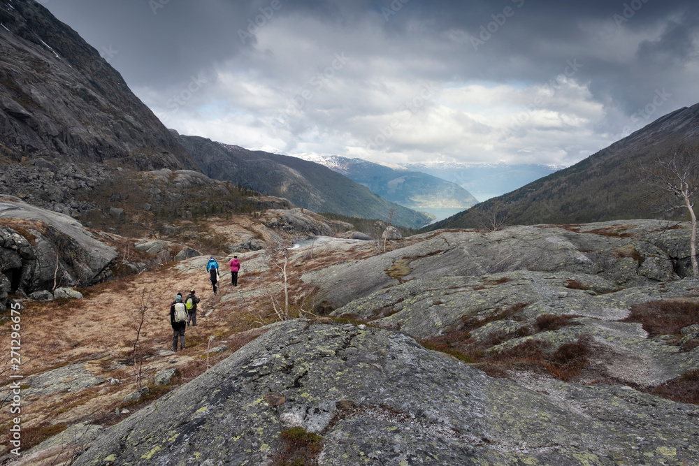 A group of people, tourists travel, walk through the national park valley of the waterfall Husedalen. Norway's landscape, High stone plateau in the mountains with a view of the sunlit fjord A group of people, tourists travel, walk through the national park valley of the waterfall Husedalen. Norway's landscape, High stone plateau in the mountains with a view of the sunlit fjord