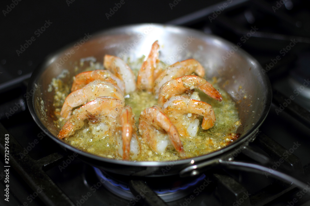 Fototapeta premium Shrimp scampi cooking in butter and garlic in a stainless steel skillet on the stove.