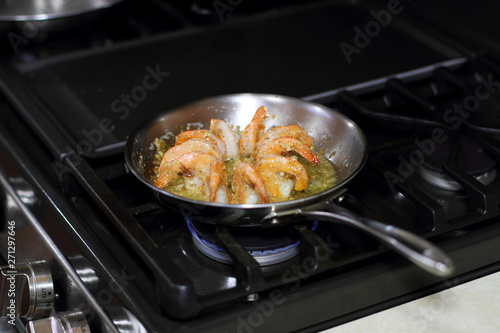 Shrimp scampi cooking in butter and garlic in a stainless steel skillet on the stove.