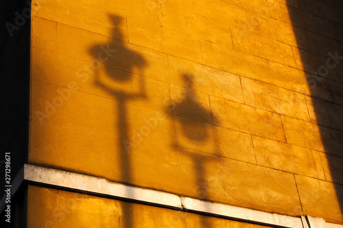 Autumnul orange sunset light casts shadow of 2 street lamps on the side of a London limestone building. photo