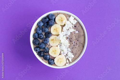 Smoothies bowl with blueberry,banana and coconut chips on the violet background.Top view.Copy space.