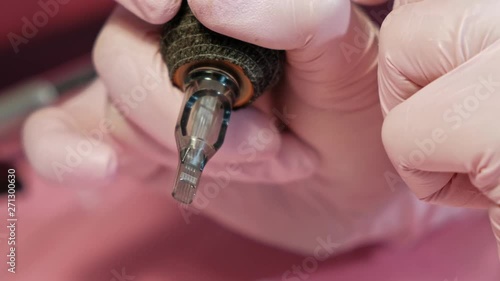 The tattoo master inserts a needle into the tattoo machine. Pink safety gloves on a red background. Female master artist.