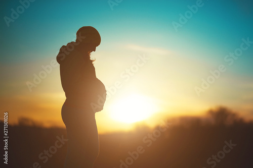 Silhouette of a future mom, pregnant woman relax in the park on a sunset background