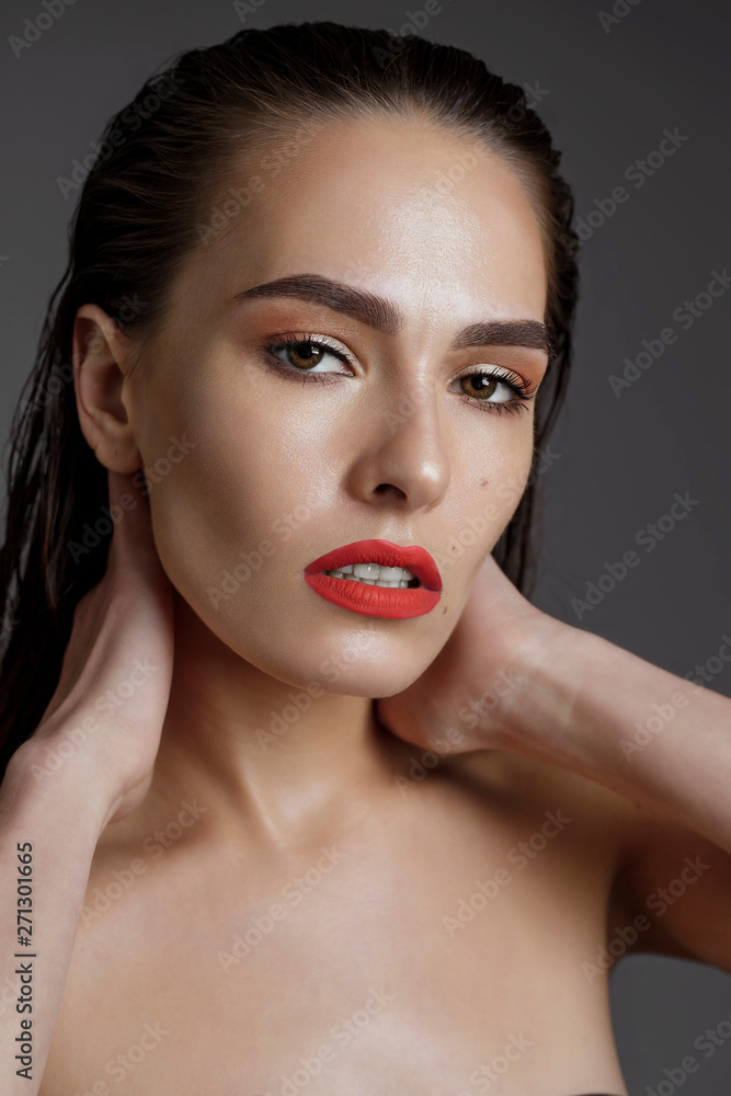 Portrait of a sexy woman with wet black hair and red lips. Professional makeup. Long hair combed up. Look into the camera, brown eyes, close-up on a gray background