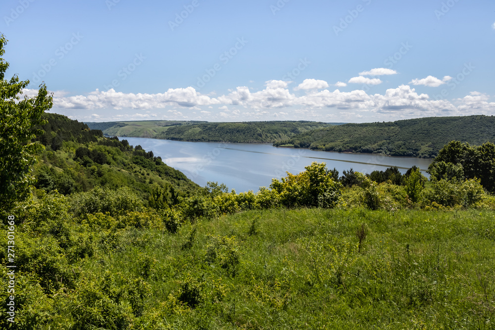 The view of the river Dniester, flowing among the high, covered with grass and forest, shores. Summer landscape. Ukraine.