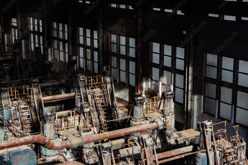 Sunlight illuminating old steel forming machinery inside a windowed warehouse, horizontal aspect