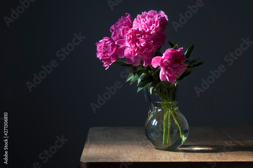 bouquet of pink peonies in a transparent vase on a dark background