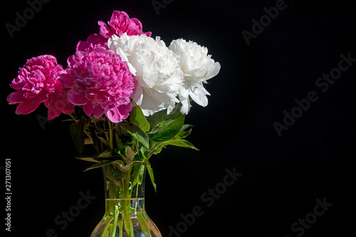 bouquet of white and red peonies in a transparent vase on a dark background