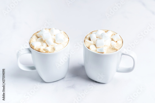 Romantic cozy desk top with two cups of coffee with marshmallows on marble table. Close-up. Space for text .