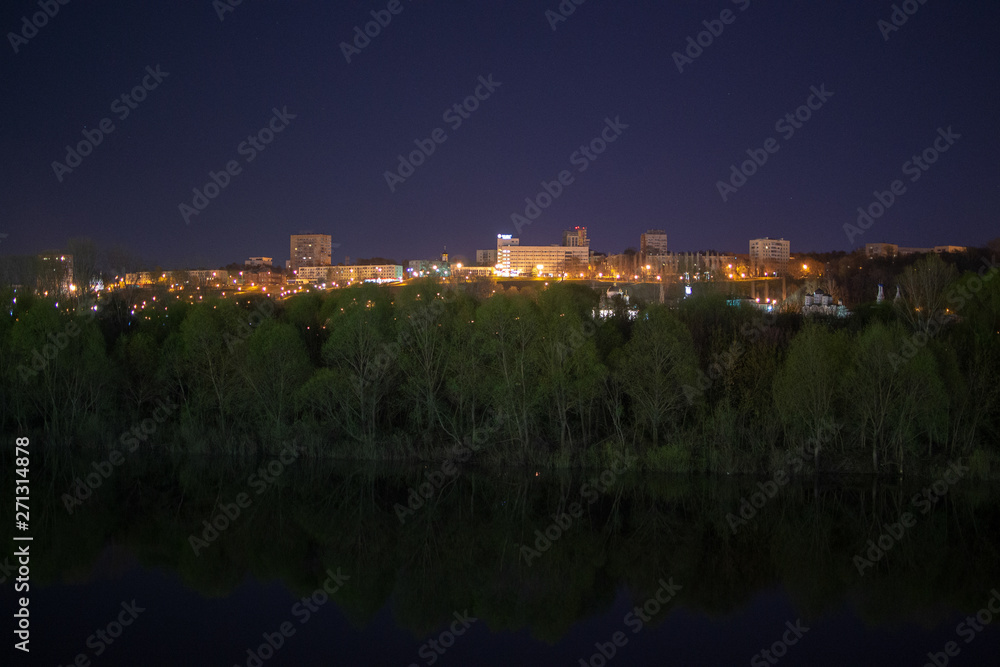 View of the night city standing by the river. Reflection of trees and bushes in the river Oka at night. Nizhny Novgorod at night.