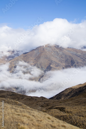 Low clouds or fog (inversion) above lake Wakatipu and Queenstown valley. View of the scenic road and snow covered peaks of Single cone, Cecil Peak and Mount Nicholas. Panoramic landscape. New Zealand.