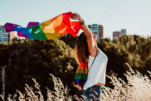 .Uoung and pretty woman proudly wearing the gay flag outdoors at sunset. Fighting for the rights and freedoms of human beings. Universal love. Lifestyle photo