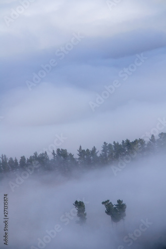 Low clouds or fog (inversion) above lake Wakatipu and Queenstown valley. View of the scenic road and snow covered peaks of Single cone, Cecil Peak and Mount Nicholas. Panoramic landscape. New Zealand.